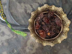 A silver bowl of kujurs, or dates, the customary fruit to end a fast in the month of Ramadan. Next to the kujurs is a green tasbih, a string of beads that is sometimes used by Muslims while making prayers.