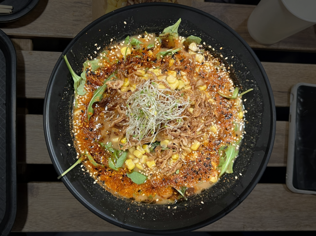 The spicy and savory Red Hot Miso ramen, topped with corn, onion, arugula, sprouts, red pepper flakes, black sesame seeds, and garlic oil. 